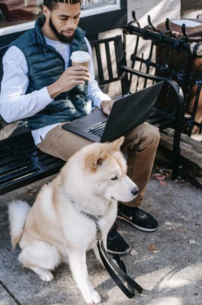 A photo of a man drinking his latte with his dog, while he's on his laptop managing his business website. The man, not the dog, silly. Although a dog on a laptop is just the best.
