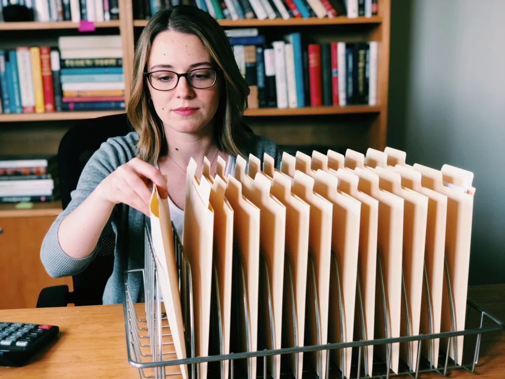 A woman with glasses sliding a blank manila folder into a neat tray of identical folders at her desk